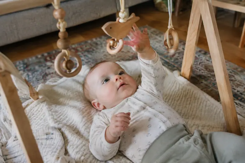Bébé allongé sous une arche d'éveil en bois avec des jouets suspendus