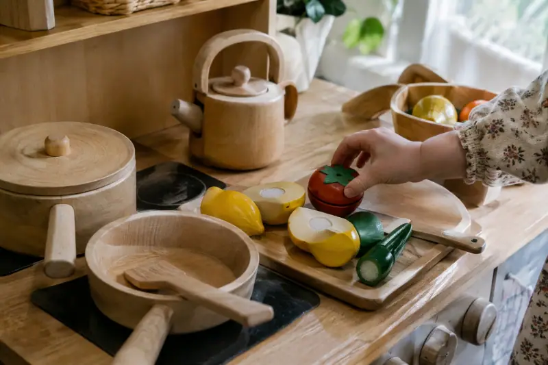 Accessoires de dinette en bois posés sur le plan de travail d'une cuisine enfant