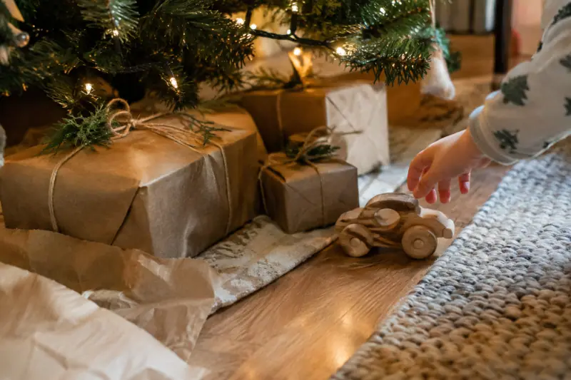 Cadeaux emballés en papier kraft avec un jouet en bois au pied du sapin