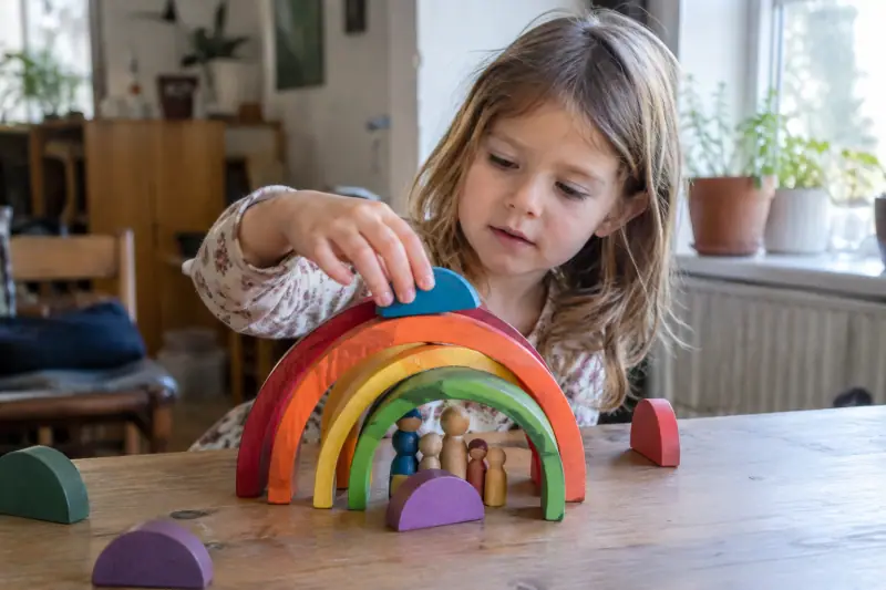 Arches en bois aux couleurs vives assemblées en petite maison par un enfant